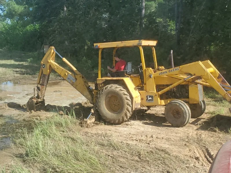 O-L Guy Farms backhoe working at the edge of a pond